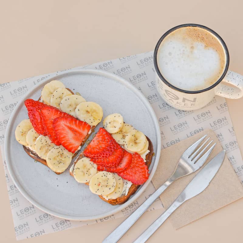 Tostadas de pan con fresas y rodajas de plátano servidas en un plato, junto a un café