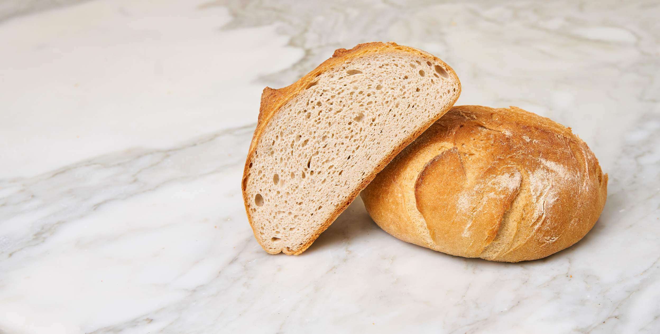 Panes artesanos, uno entero y otro cortado por la mitad, sobre una superficie clara